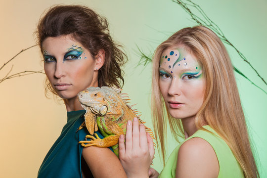 Wild animal in the hands of man. Two girls with an unusual make-up and with an iguana in their hands. Animal out of it. An image of a female predator and snake