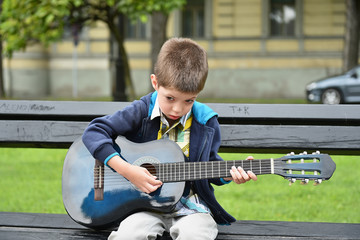 child boy playing on guitar in a park