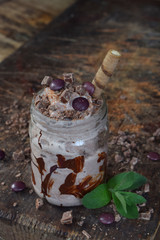 Homemade coffee ice cream with black chocolate in jar on wooden background. Side view. Space for text. Photographed with natural light.