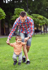 Fototapeta na wymiar baby boy taking first steps with father help in a park