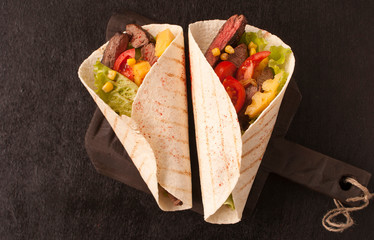 Mexican tacos with beef, vegetables and pineapples and corn grains on a wooden kitchen Board. Taco al pastor on a wooden Board on a black background. Top view with copy space