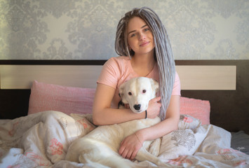 Attractive light ash dreadlocks young girl  with dog while laying on a bed 