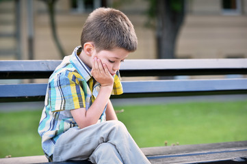 sad child boy sitting on a bench