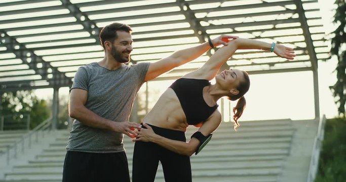 Young beautiful Caucasian woman ding workout at the stadium on a summer day and male trainer or her boyfriend teaching her.