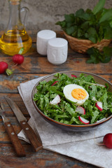 Vitamin salad from lettuce, radish, green onions and eggs, seasoned with vegetable oil in plate on wooden background. Healthy food. Salad of fresh green vegetables