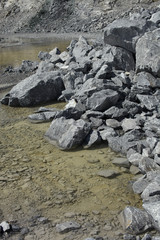 Small spring lake and a pile of limestone at the bottom of the quarry. Mining industry.
