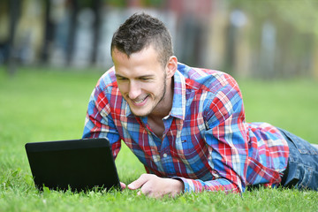 young student man with laptop lying on grass