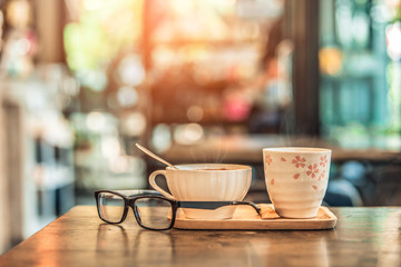 Hot coffee glass cup with glasses on wooden table in coffee shop. Vintage tone