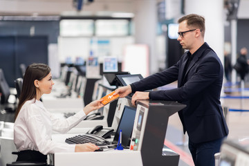 Business trip. Handsome young businessman in suit holding his passport and talking to woman at airline check in counter in the airport