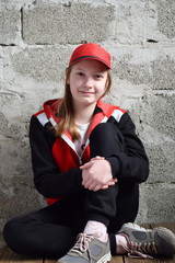 Young girl is sitting in black sports suit, red cap and smiling. Concept portrait of a pleasant friendly happy teenager.
