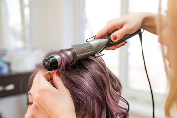 Close up of stylist's hand using curling iron for hair curls 