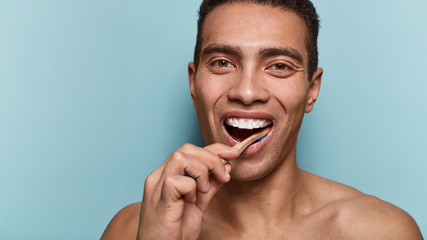 Cropped shot of happy smiling man has white teeth, cleans with toothbrush, wakes up early in morning, isolated over blue background with blank space for your advertising content. Hygiene concept