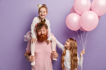 Childhood and fatherhood concept. Red haired dad rides piggyback for little daughter, entertains children on birthday party. Small child gives air balloons for friend, feel happiness, isolated