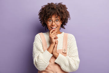 Image of optimistic female student has Afro hairstyle, smiles at camera, enjoys weekened, expresses...