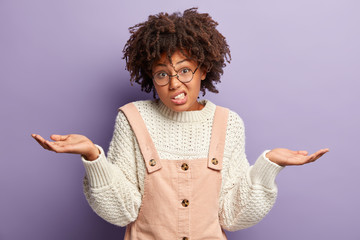 Hmm, what to choose? Unaware good looking woman has curly hair, raises hands, feels doubt, wears...