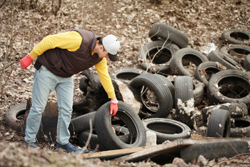 Volunteer removes car tires from the park. Environmental pollution, outdoor trash and rubbish.