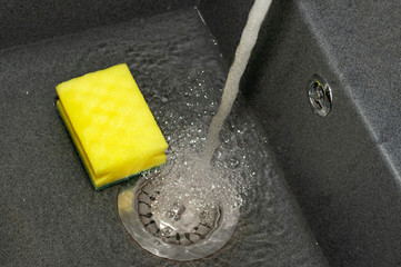 Yellow sponge for dishes in a dark shell. Water is collected in the sink. Close-up. Cleaning,...