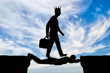 Selfish man with a crown on his head is walking over a man in the form of a bridge over an abyss