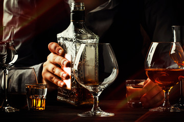 The bartender pours the cognac or brandy in big wine glass on the old bar counter. Vintage wooden background in pub or bar, night mood. Place for text, toning, selective focus
