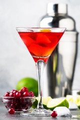 Cosmopolitan cocktail with vodka, liqueur, cranberry juice, lime, ice and orange zest, gray bar counter background, bartender tools, copy space