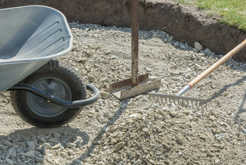 Schubkarre, Handverdichter und Harke beim Wegebau