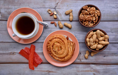 Sweet bun. Cup of tea. Peanuts. Walnuts. Wood background. Heap of nuts. Dried fruits. Fall. Top view. Rustic.  Still life.