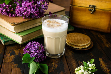 Delicious latte macchiato, biscuits, old books and lilac flowers on a wooden table
