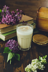 Delicious latte macchiato, biscuits, old books and lilac flowers on a wooden table