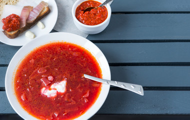 plate of borscht, ketchup, lard on a piece of bread on a wooden gray background