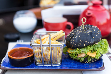 Black burger with fried potatoes and ketchup on a blue plate