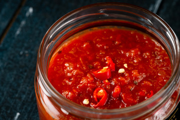 Homemade red hot chili pepper sauce in a glass bowl on a dark wooden background, seasoning for meat dishes