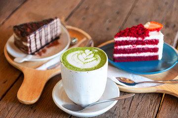 Hot green tea matcha latte with red velvet soft cake and chocolate cake on a wooden table at the coffee shop.