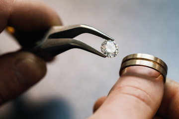 Jeweler tries on a precious stone in a gold blank for the future of the ring, closeup