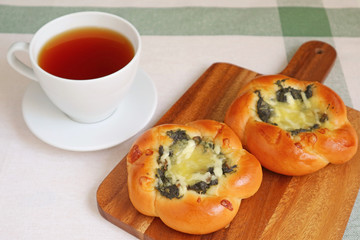 Pair of spinach and cheese buns with a cup of hot tea on white table