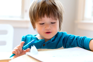 Happy toddler boy drawing at his desk