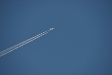 Commercial aircraft at very high altitude with white contrail on cloudless blue sky