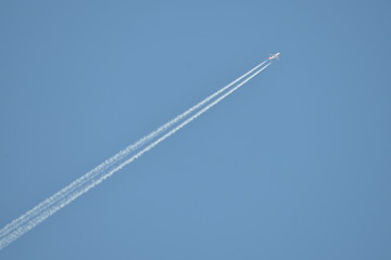 Commercial aircraft at very high altitude with white contrail on cloudless blue sky