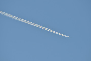 Commercial aircraft at very high altitude with white contrail on cloudless blue sky
