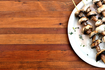 Mushrooms on wooden skewers in a white plate   on a wooden table.