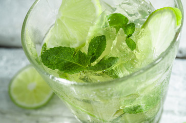 Mojito cocktail with slices of lime and mint leaves in highball glass on a wood table. White background.