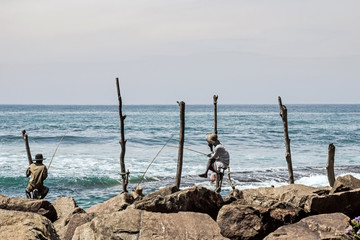 fisher man sitting on wood stick at coast in Mirissa, Sri Lanka 