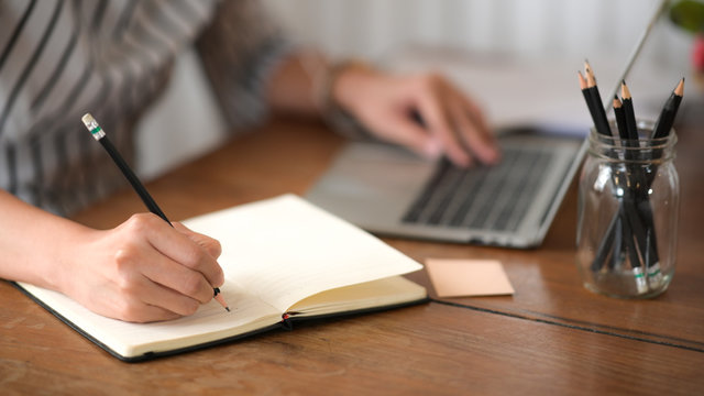 Businesswoman writing note while using laptop at table in office