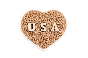 Wheat grains lie in a heart-shaped plate. USA from wooden letters on the grain. Isolated on white. The concept of import and export, food reserves, the love of bread in America.