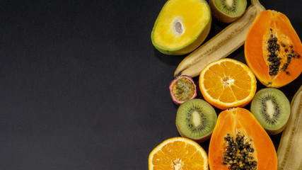 A set of fruits, fruit is on the right and free space left, black background, pineapple orange, banana, lime, kiwi, mango, lemon, papaya, ginger, exotic