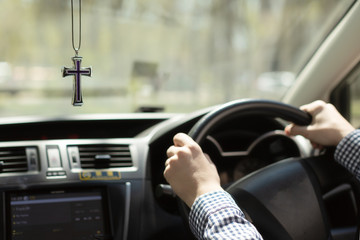 Catholic cross in the car . men's hands on the steering wheel in the car on the background of the Christian cross