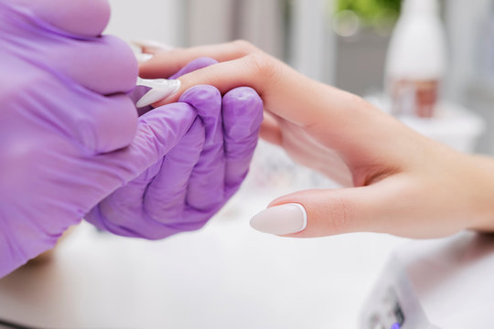 Manicurist work on a woman client hands, make her nails look beautiful. Salon procedure in process. Professional works in gloves for sterility