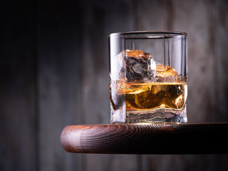 Glass of whiskey with ice cubes on the wooden table with wooden background