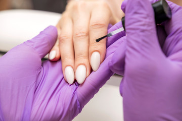 Obraz na płótnie Canvas Manicurist work on a woman client hands, make her nails look beautiful. Salon procedure in process. Professional works in gloves for sterility