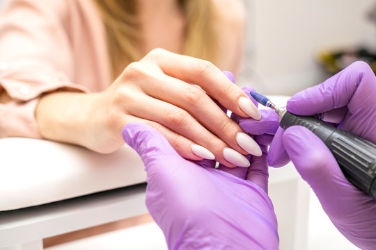 Manicurist work on a woman client hands, make her nails look beautiful. Salon procedure in process. Professional works in gloves using drill for sterility