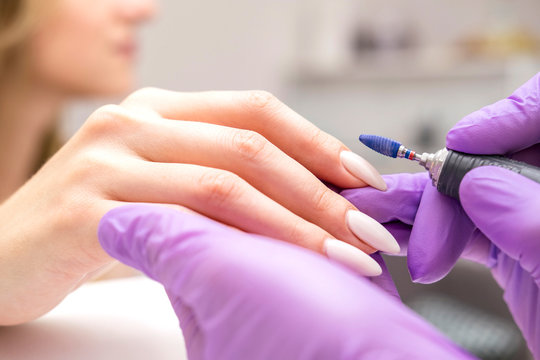 Manicurist work on a woman client hands, make her nails look beautiful. Salon procedure in process. Professional works in gloves using drill for sterility